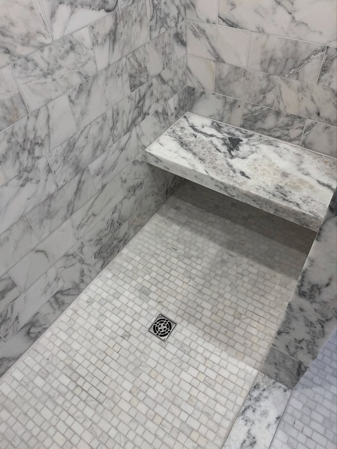 Shower with a floating marble slab bench and brick-set mosaic floor