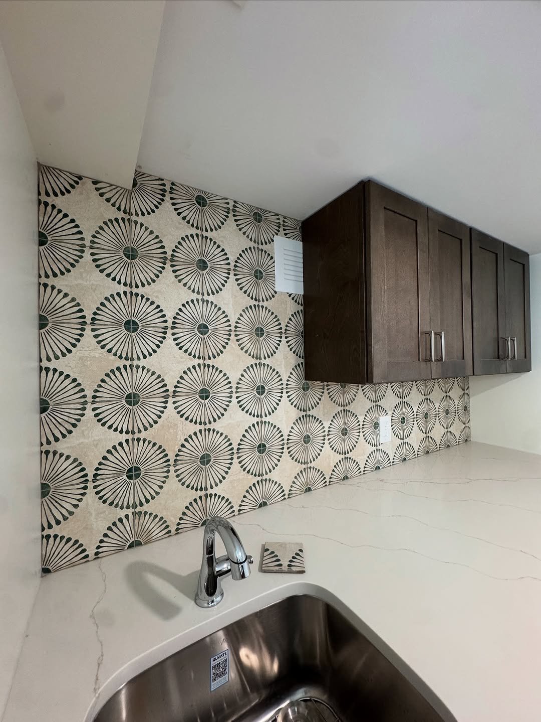 Kitchen with a cream and green starburst tile backsplash, dark cabinets, and quartz counters